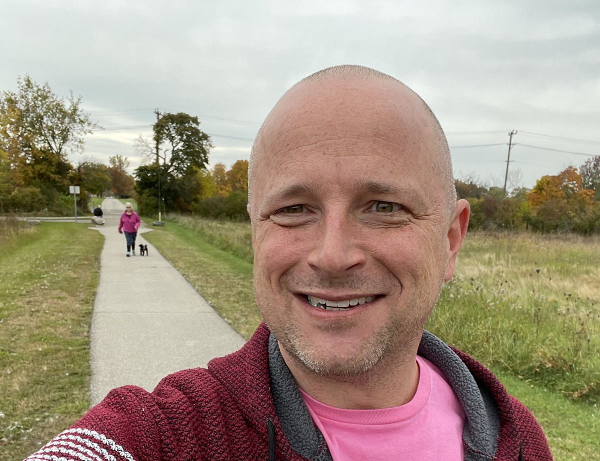 Jessie Heath on a fall trail walk — cardigan, pink tee, big smile